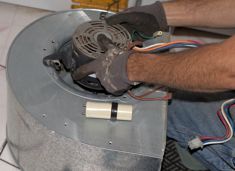 A picture of a furnace blower motor with two hands installing.