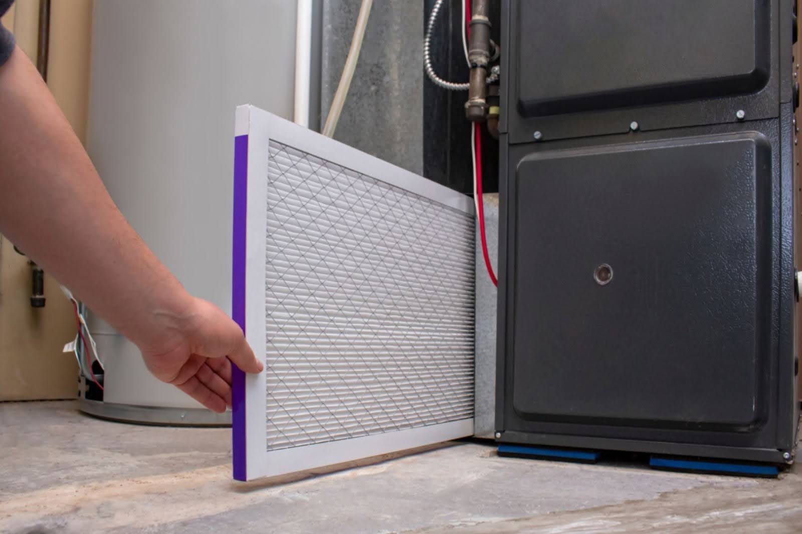 A man removing a dirty air filter from a furnace.