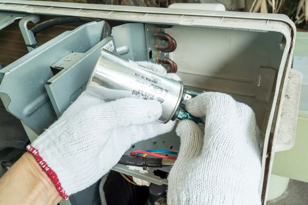 An HVAC technician is professionally installing an AC capacitor.